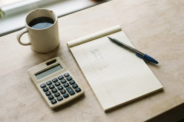 A notepad, calculator and pen on a desk for working out a bare minimum budget