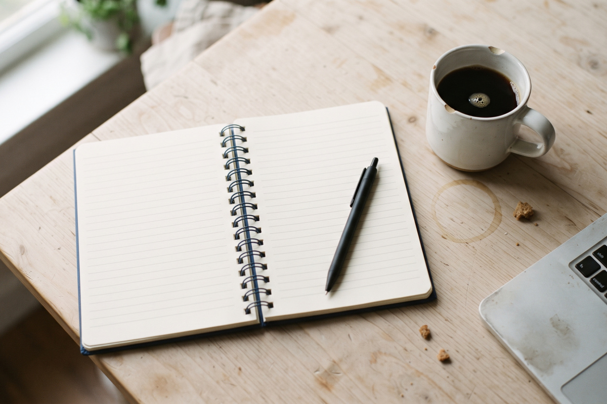Notebook, pen and laptop on a kitchen table for budgeting with an irregular income